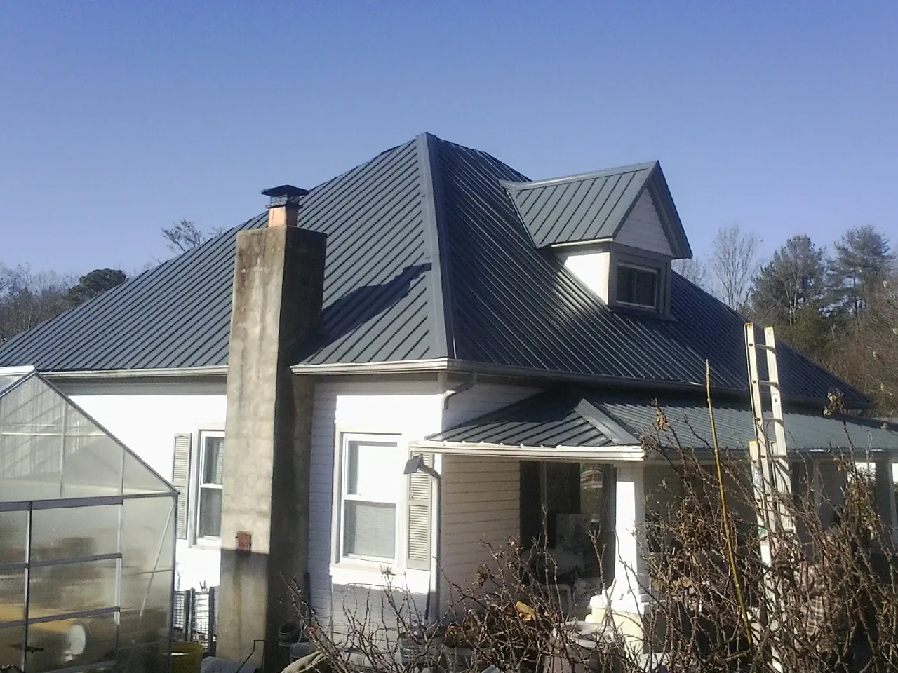 Dark blue standing seam metal roof on a white farmhouse with dormer — Slate & Tile Roof Repair by Roofing Brothers in Laingsburg