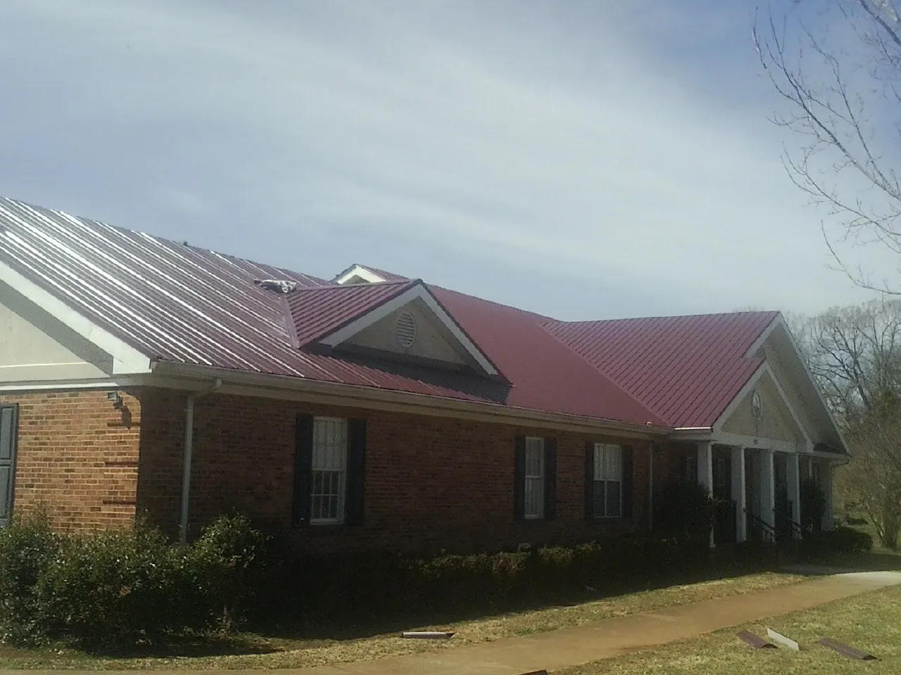 Red metal roof with gabled entries on a long brick building, from a Hail Damage Roof Repair job in Laingsburg