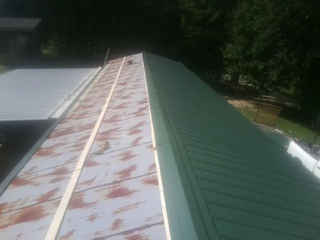 Old rusted panels beside newly installed green metal roofing — Wind Damage Roof Repair by Roofing Brothers in Laingsburg