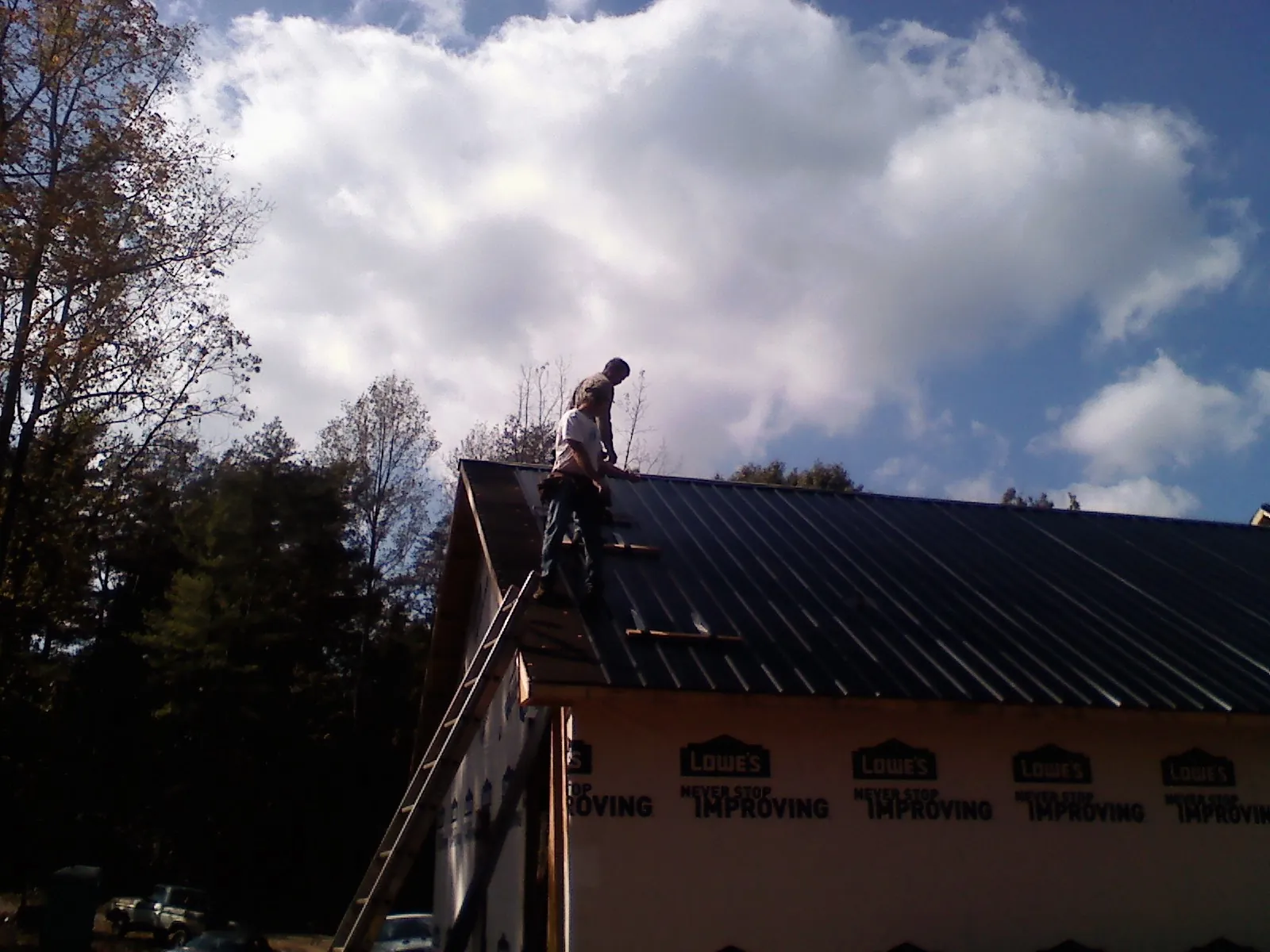 Roofer fastening dark metal panels high against a cloudy sky, from a Roof Inspection job in Laingsburg