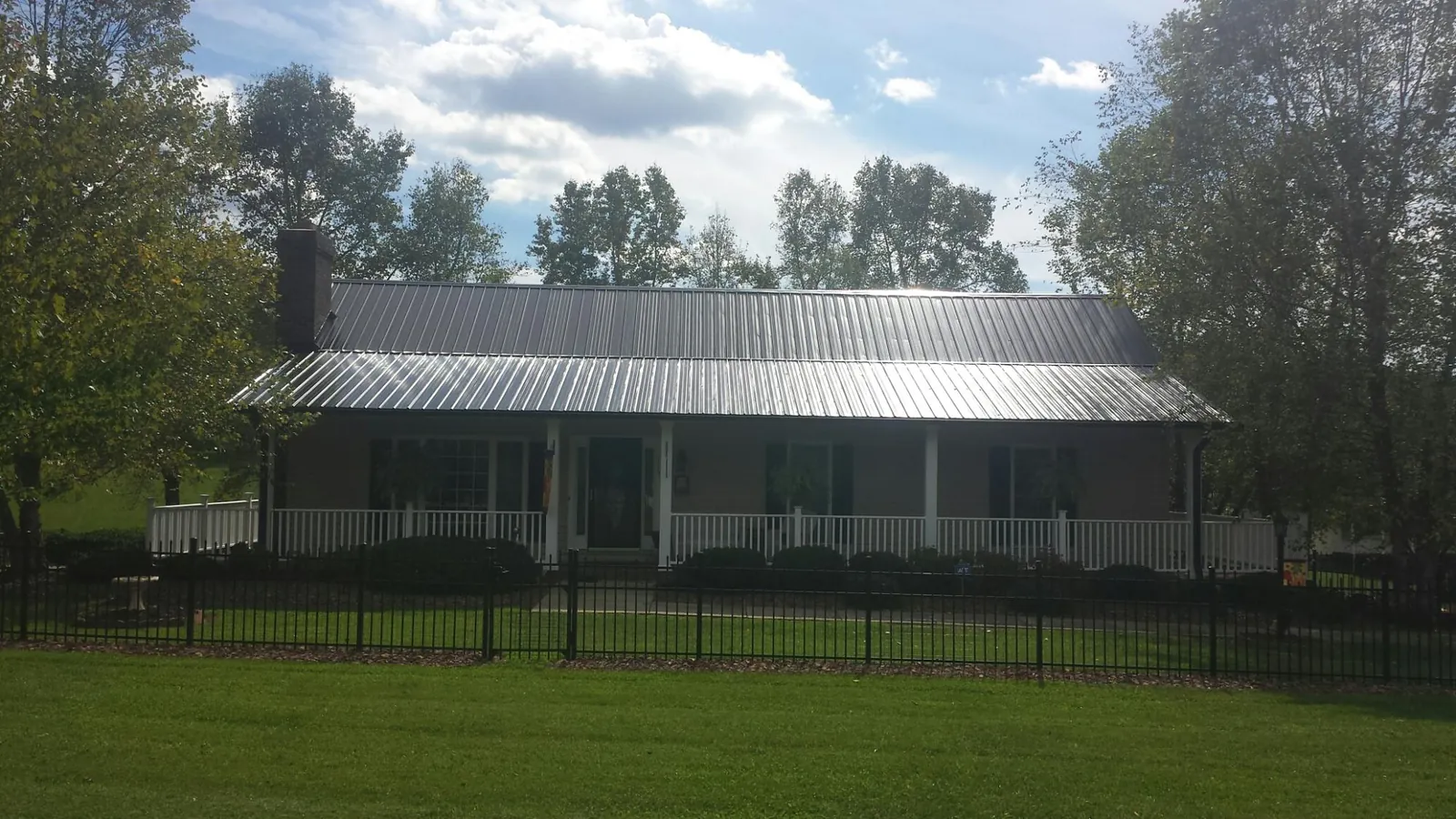 Gray metal roof on a brick ranch with a full width front porch — Gutter Guard Installation work by our crew in Laingsburg