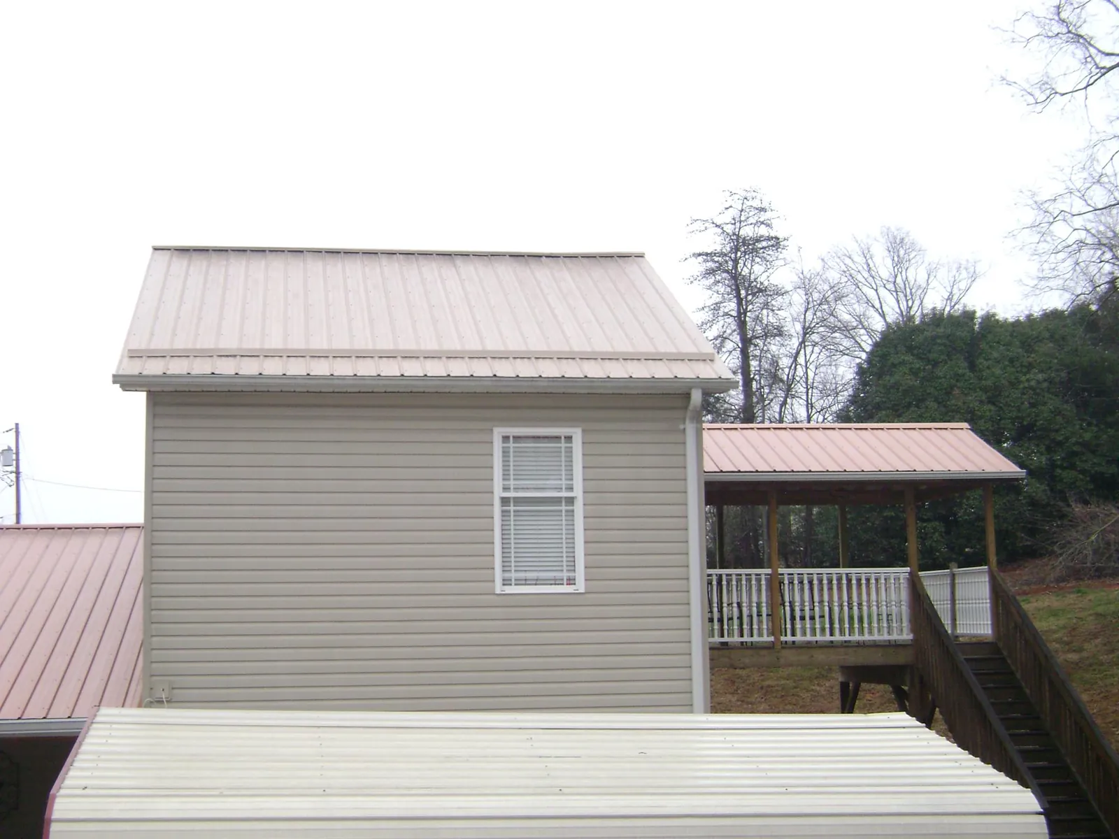 Tan metal roofs on a two story addition and attached porch, from a Roof Replacement job in Laingsburg
