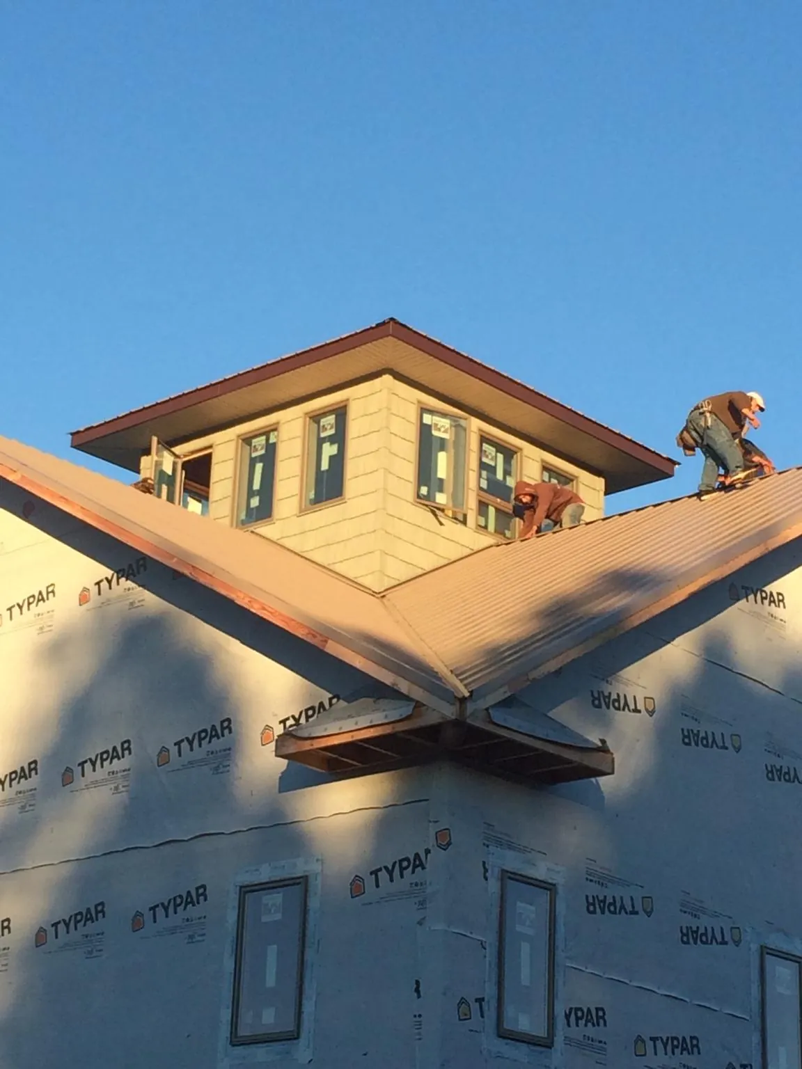 Roofers working around a rooftop cupola on a new metal roof at sunset — Roof Waterproofing in Laingsburg by Roofing Brothers